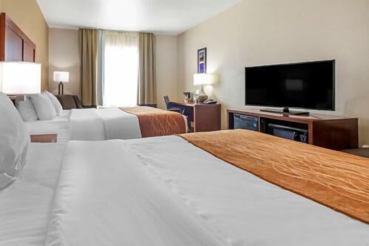 A hotel room with two beds, a television, a desk, and a chair.