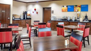 A hotel dining area with red upholstered chairs, wooden tables, and a buffet counter with food displays. - Comfort Inn Near UNT (Denton)