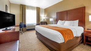 A hotel room with a large bed, a desk with a flat-screen TV, a chair, a lamp, and a nightstand. - Comfort Inn Near UNT (Denton)
