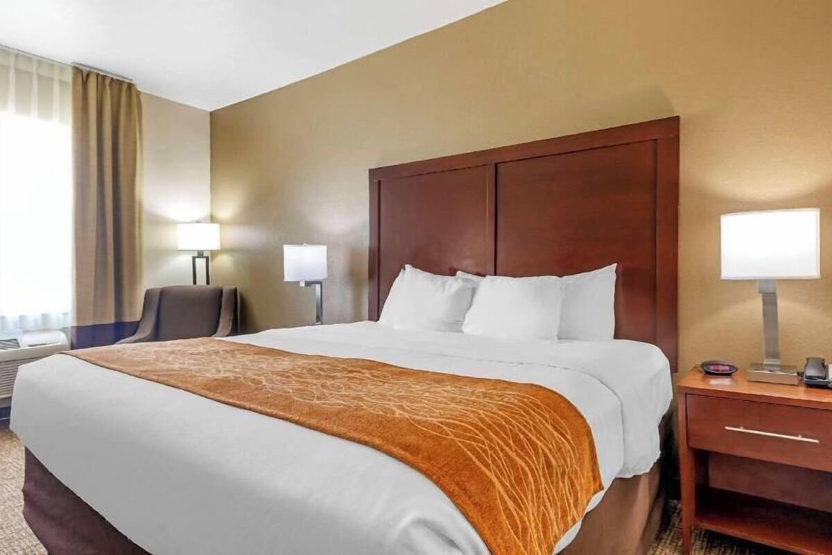 A hotel room with a large bed, two bedside tables, a chair, and a lamp.