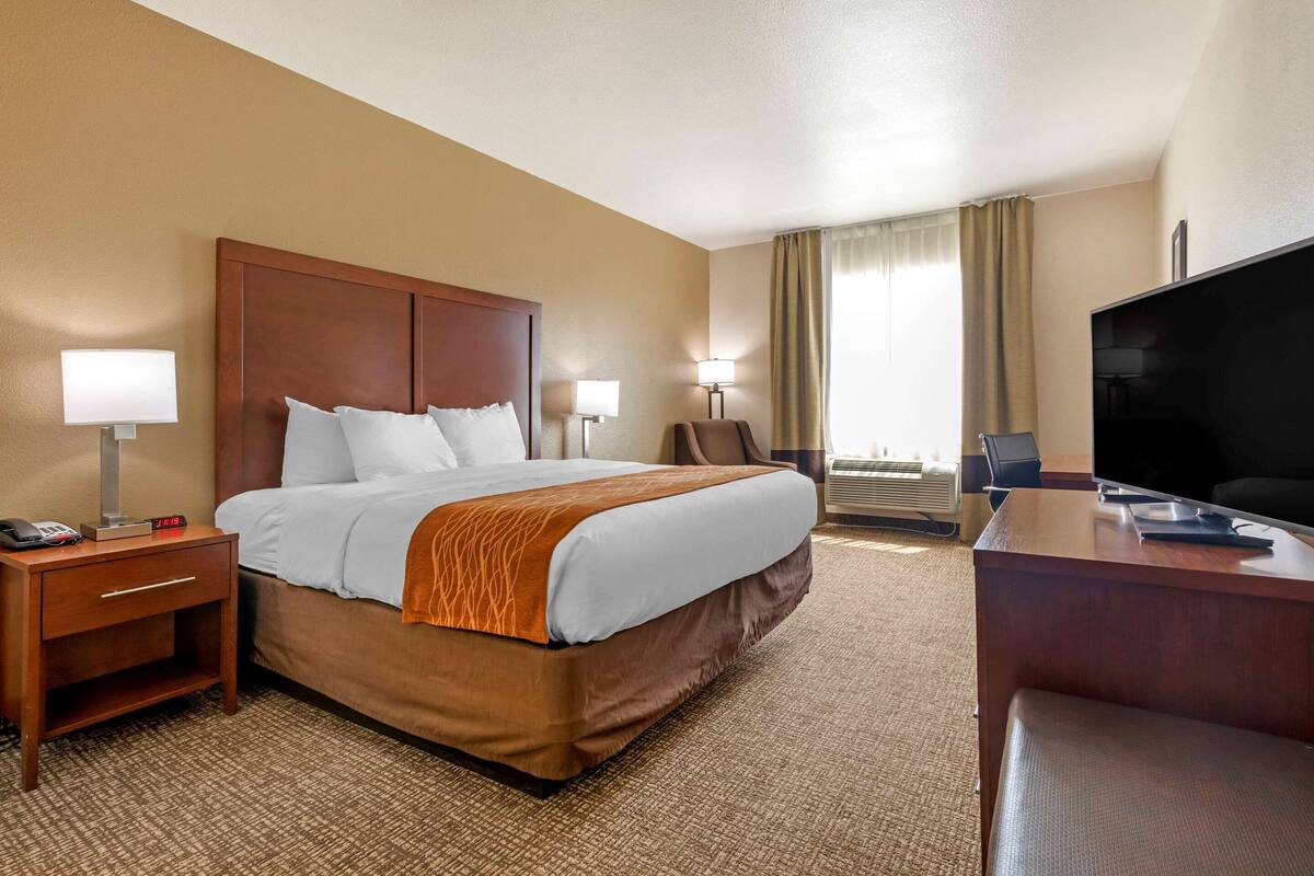 A hotel room with a large bed, a desk with a flat-screen TV, two bedside lamps, a chair, and a desk lamp.