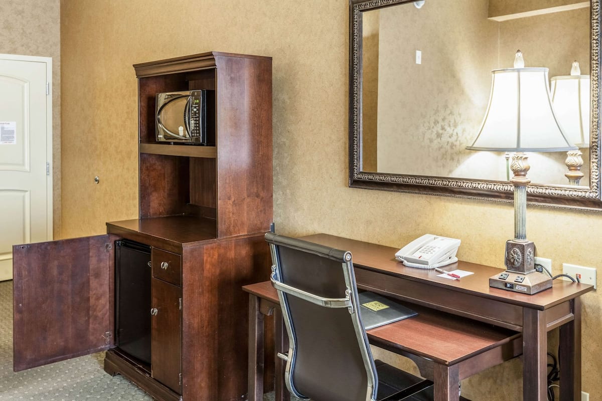 Une chambre d’hôtel avec un bureau en bois, une chaise, un téléphone, une lampe et un miroir.
