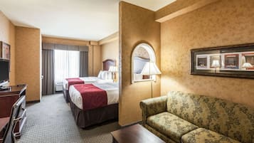 A hotel room with two beds, a sofa, a desk, and a TV.