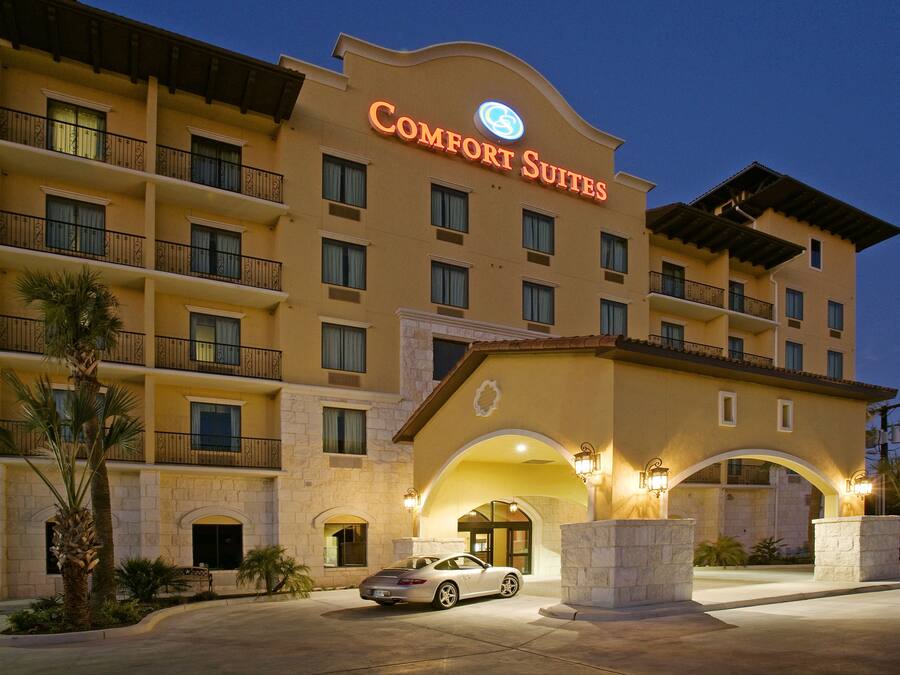 Un hotel con un cartel que dice "Comfort Suites", con varios balcones, fachada de piedra y un coche estacionado al frente.