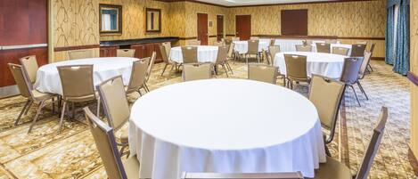 Un salón de conferencias con mesas y sillas redondas, suelo alfombrado y paredes con diseño.