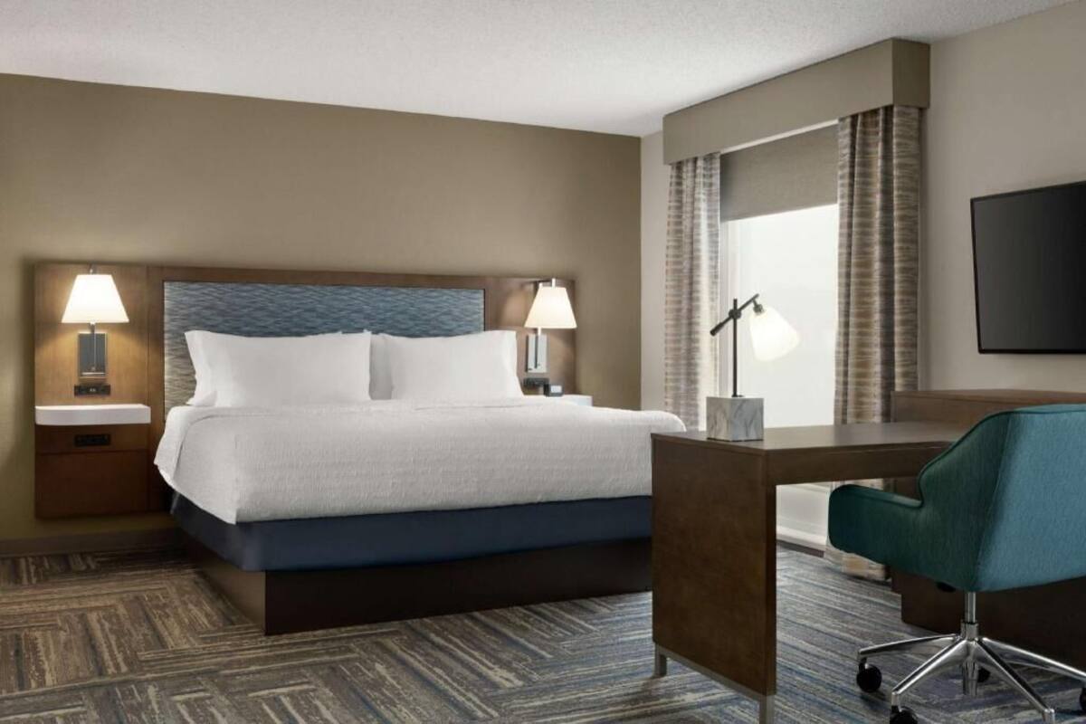 A hotel room with a bed, bedside lamps, a desk, a chair, and a TV.