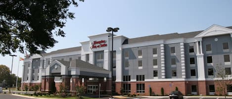 A Hampton Inn & Suites hotel with a modern facade, a covered entrance, and a parking lot.