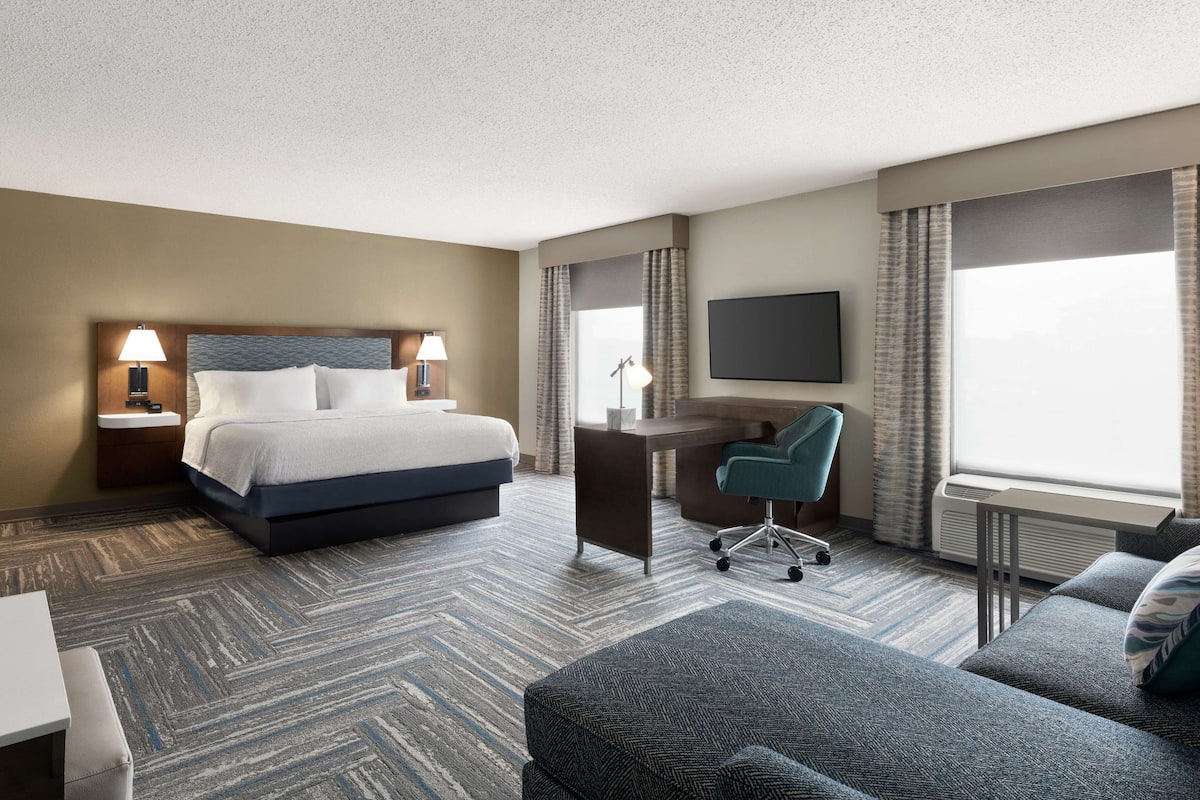 A hotel room with a bed, desk, chair, and a TV.