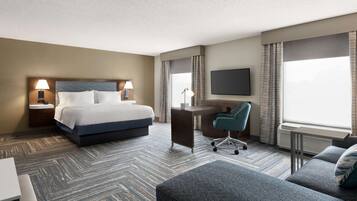 A hotel room with a bed, desk, chair, and a TV.