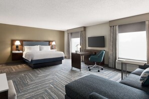 A hotel room with a bed, desk, chair, and a TV.