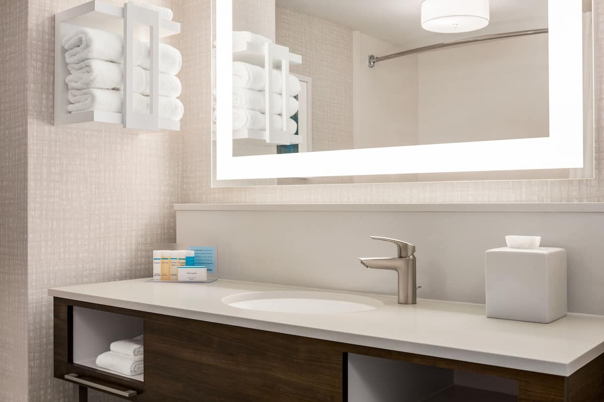 A modern bathroom with a large mirror, white sink, and towel storage.