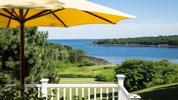 A coastal view with a white fence, a yellow umbrella, and a golf course. - Strawberry Hill Seaside Inn (Rockport)