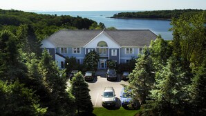 A large house with a garage and a driveway, surrounded by trees and a body of water. - Strawberry Hill Seaside Inn (Rockport)