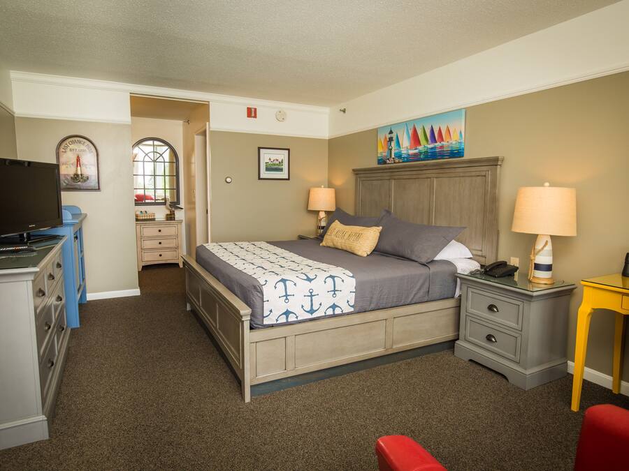 A bedroom with a bed, two bedside tables, a desk, a chair, and a TV.