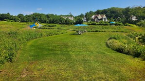 A lush green landscape with a pathway leading to a seating area with blue umbrellas. - Strawberry Hill Seaside Inn (Rockport)