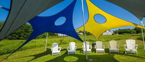 A shaded outdoor area with white Adirondack chairs arranged in a row.