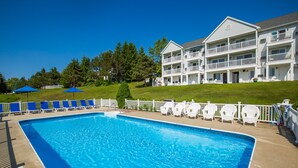 A rectangular swimming pool with a clear blue water, surrounded by white lounge chairs and umbrellas, and a white building with balconies in the background. - Strawberry Hill Seaside Inn (Rockport)