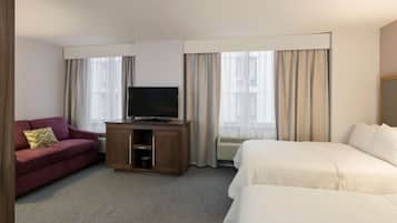 Habitación de hotel con cama, televisor sobre un soporte de madera, sofá rojo y ventana con cortinas.