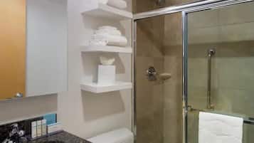 A bathroom with a glass shower enclosure, white shelves with towels, and a marble countertop.