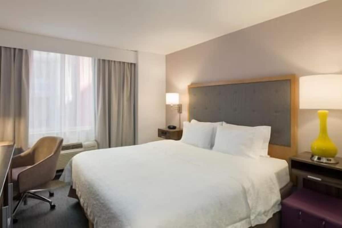 A hotel room with a large bed, a chair, a desk, a lamp, and a window with curtains.