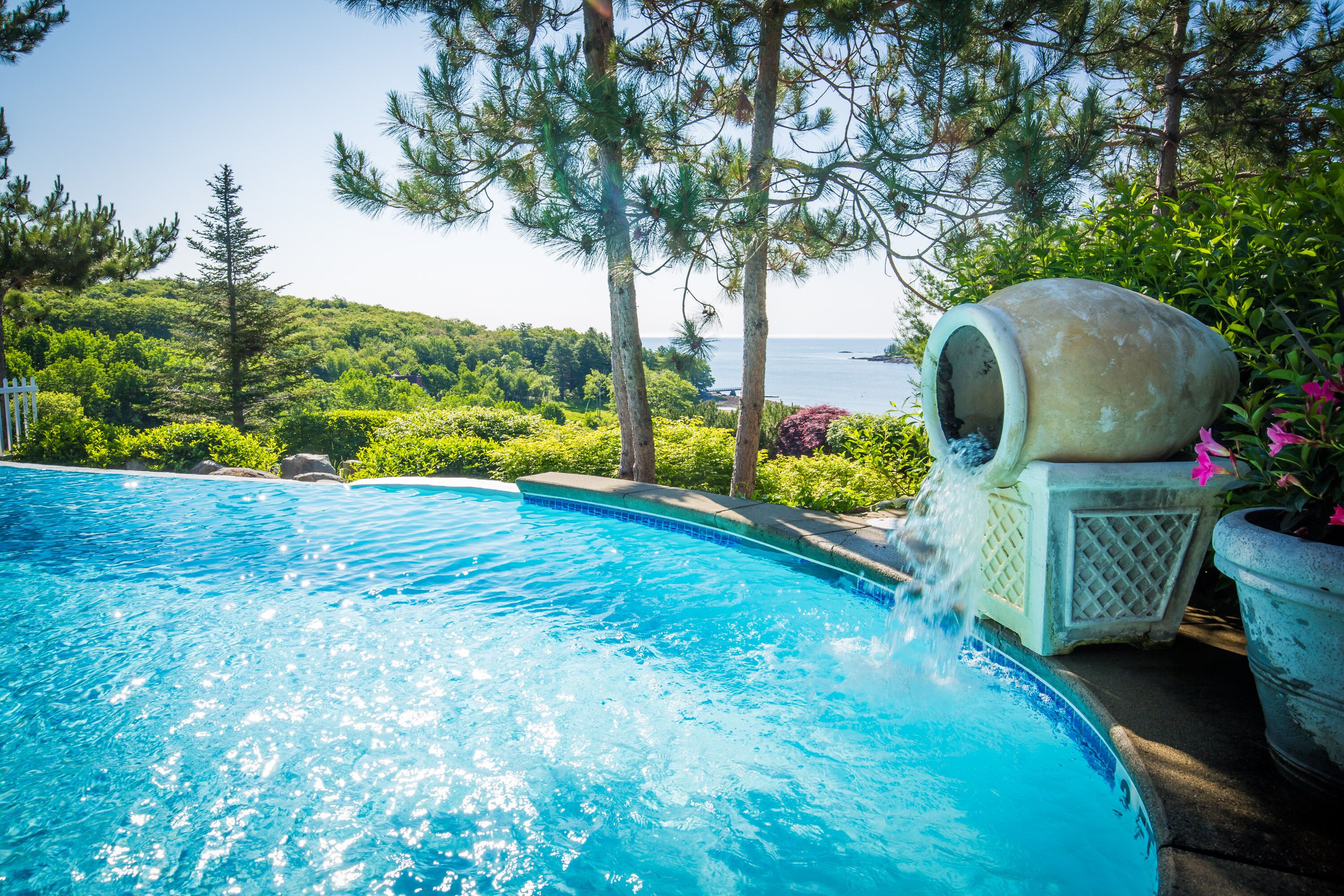 A swimming pool with clear blue water, surrounded by lush greenery and a view of the sea.