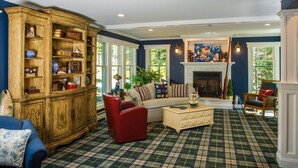 A cozy living room with a plaid carpet, a wooden cabinet with various items, a sofa, and a fireplace.