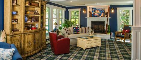 A cozy living room with a plaid carpet, a wooden cabinet with various items, a sofa, and a fireplace.