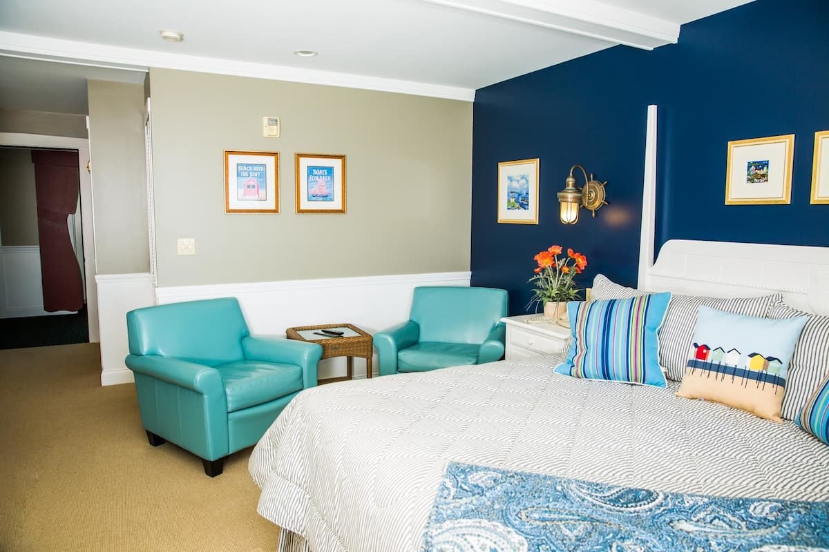 A hotel room with a bed, two matching armchairs, a small table, and a nightstand with a lamp.