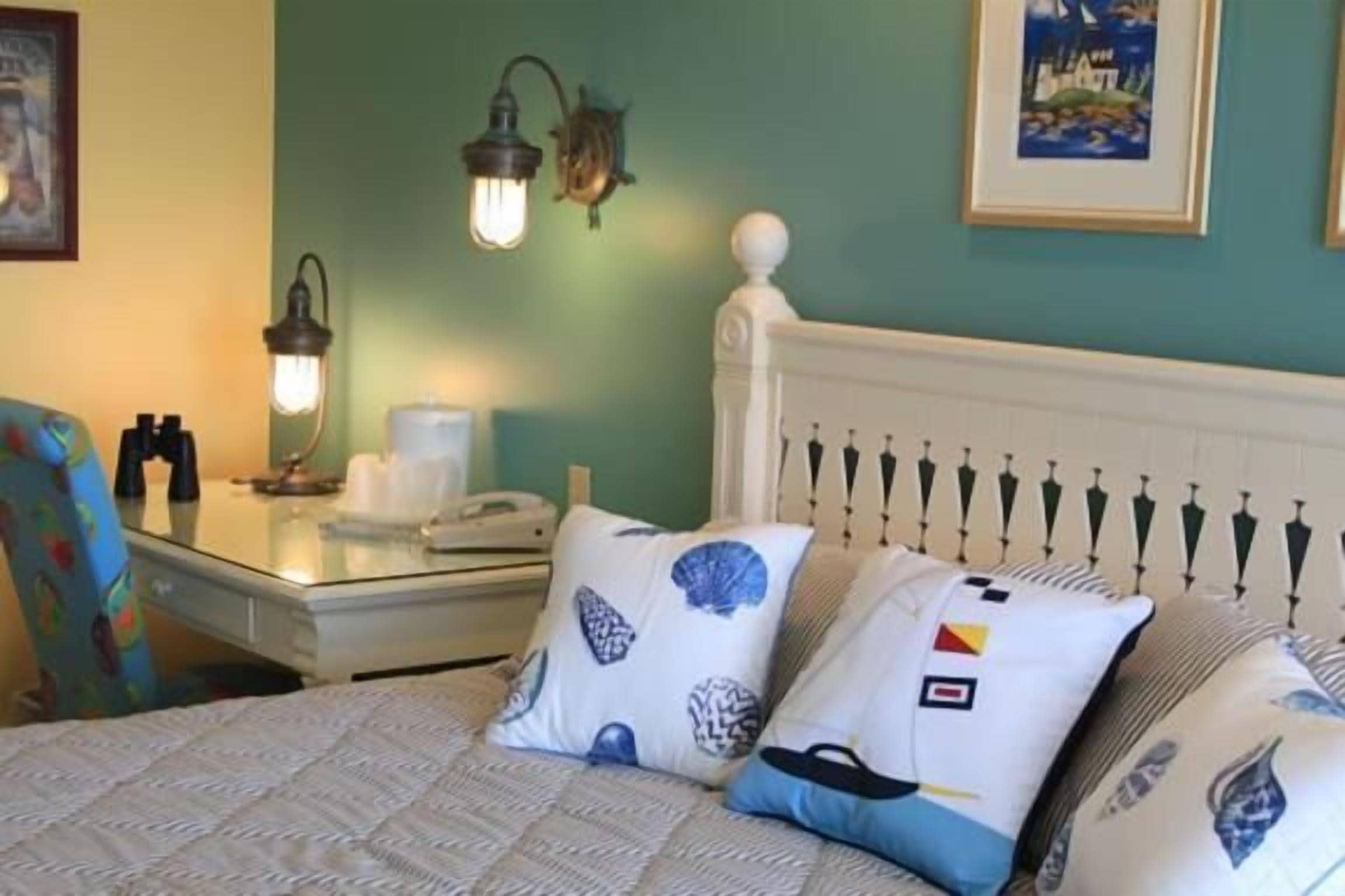 A neatly made bed with patterned pillows, a bedside table with a lamp, and a framed picture on the wall.