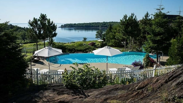 A swimming pool with umbrellas, surrounded by a white fence, and a view of a lake.