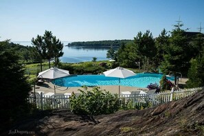 A swimming pool with umbrellas, surrounded by a white fence, and a view of a lake.