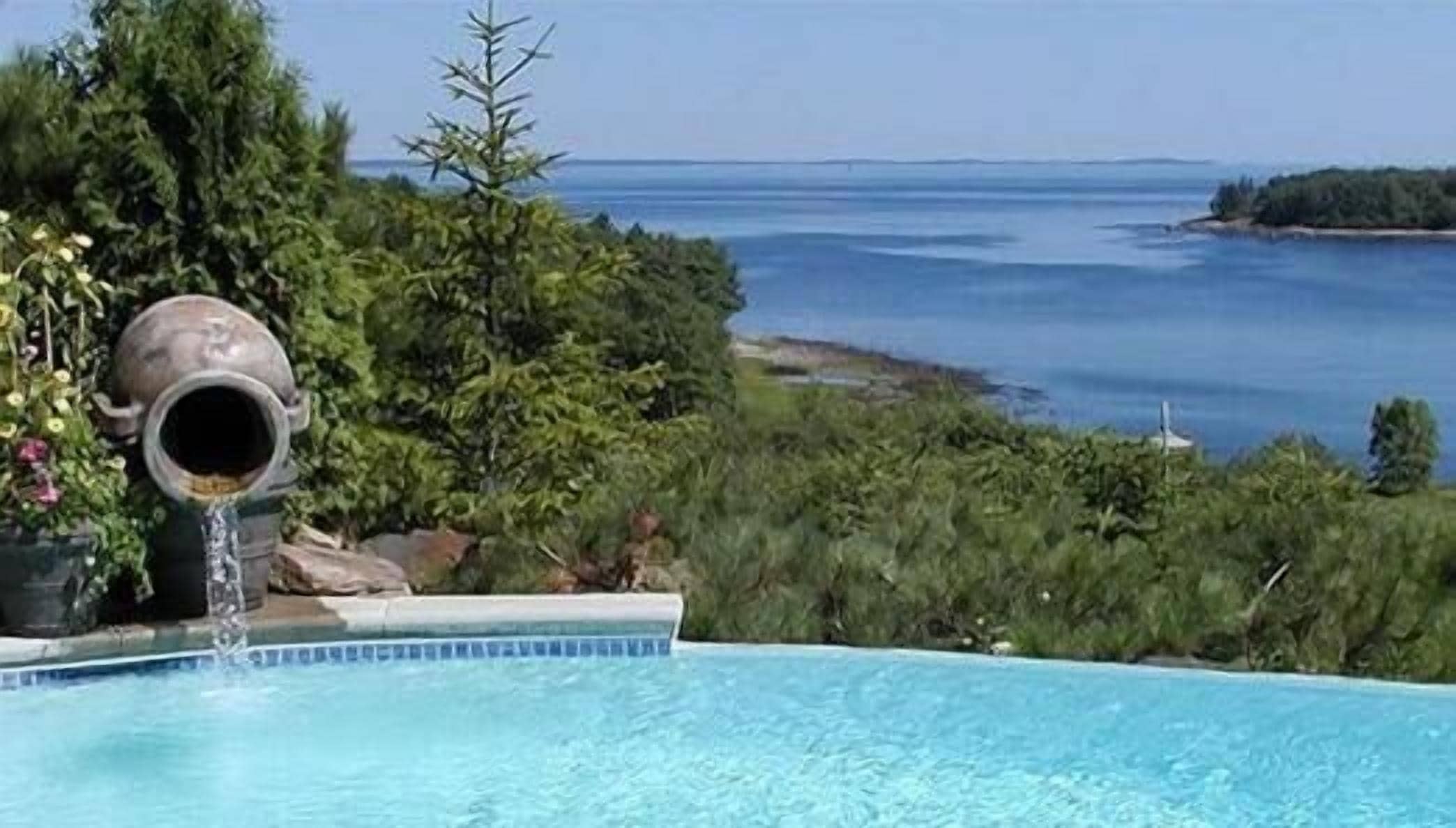 A swimming pool with a clear view of the ocean and a rocky shoreline.