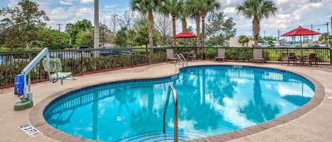 A swimming pool with a metal ladder, surrounded by palm trees and a red umbrella.