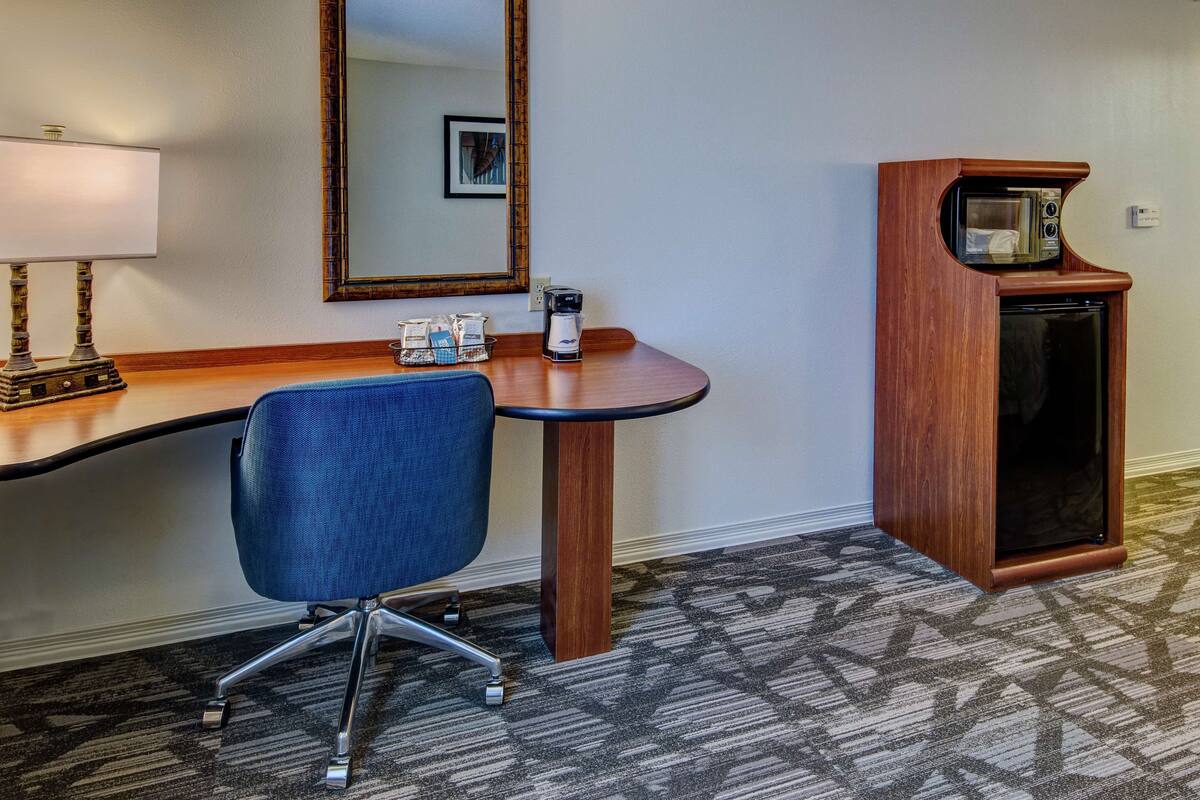 Une chambre d’hôtel avec un bureau en bois, une chaise bleue, un four à micro-ondes et une machine à café.
