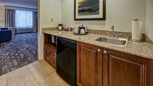 A hotel kitchen with granite countertops, a dishwasher, wooden cabinets, a sink, and a framed picture above the sink. - Hampton Inn & Suites Stuart-North (Stuart)