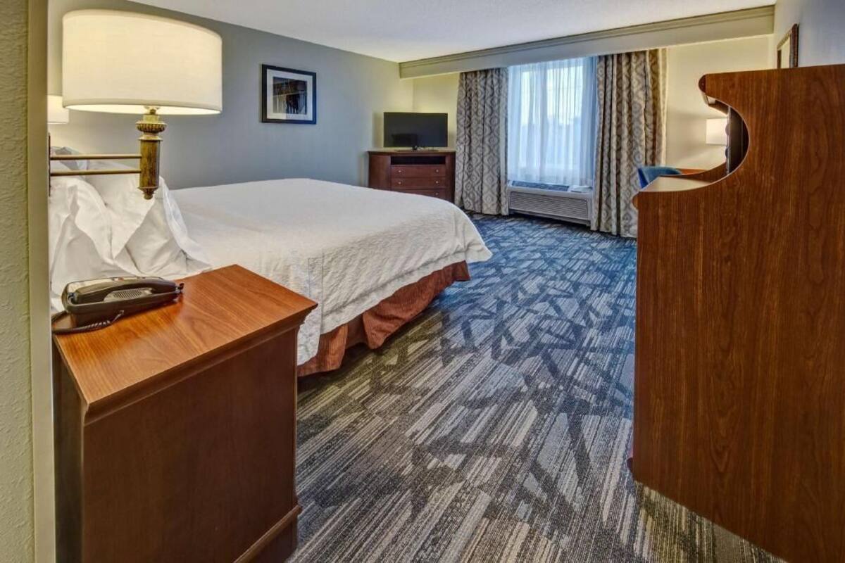 A hotel room with a bed, a desk with a telephone, a television, a dresser, and a window with curtains.