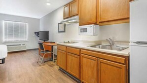 Cocina compacta con armarios de madera, microondas, pileta y un escritorio con silla.