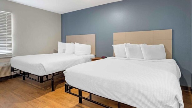Habitación de hotel con dos camas, una ventana con persianas, suelo de madera y una lámpara en el techo.