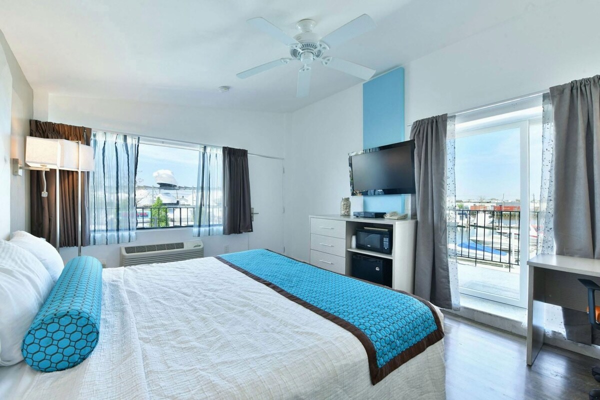 Habitación de hotel con cama, televisión, escritorio y balcón con vistas.