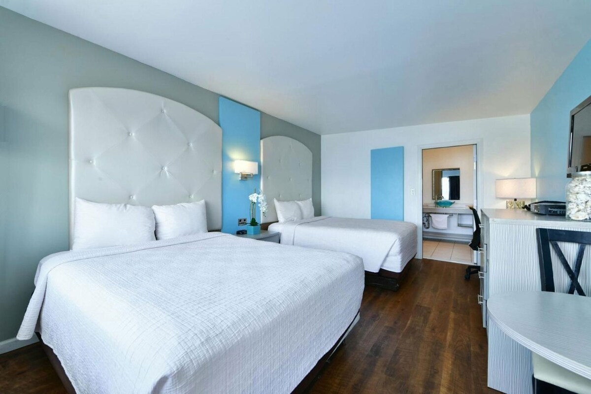 A hotel room with two beds, a desk, and a bathroom visible through an open door.