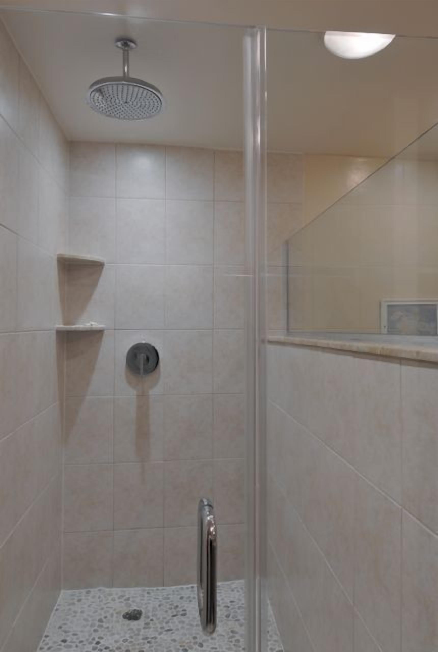 A shower area with a glass door, a showerhead, and a tiled floor.