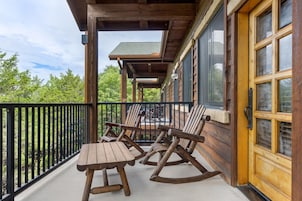 A wooden deck with two rocking chairs and a table, overlooking a forested area.