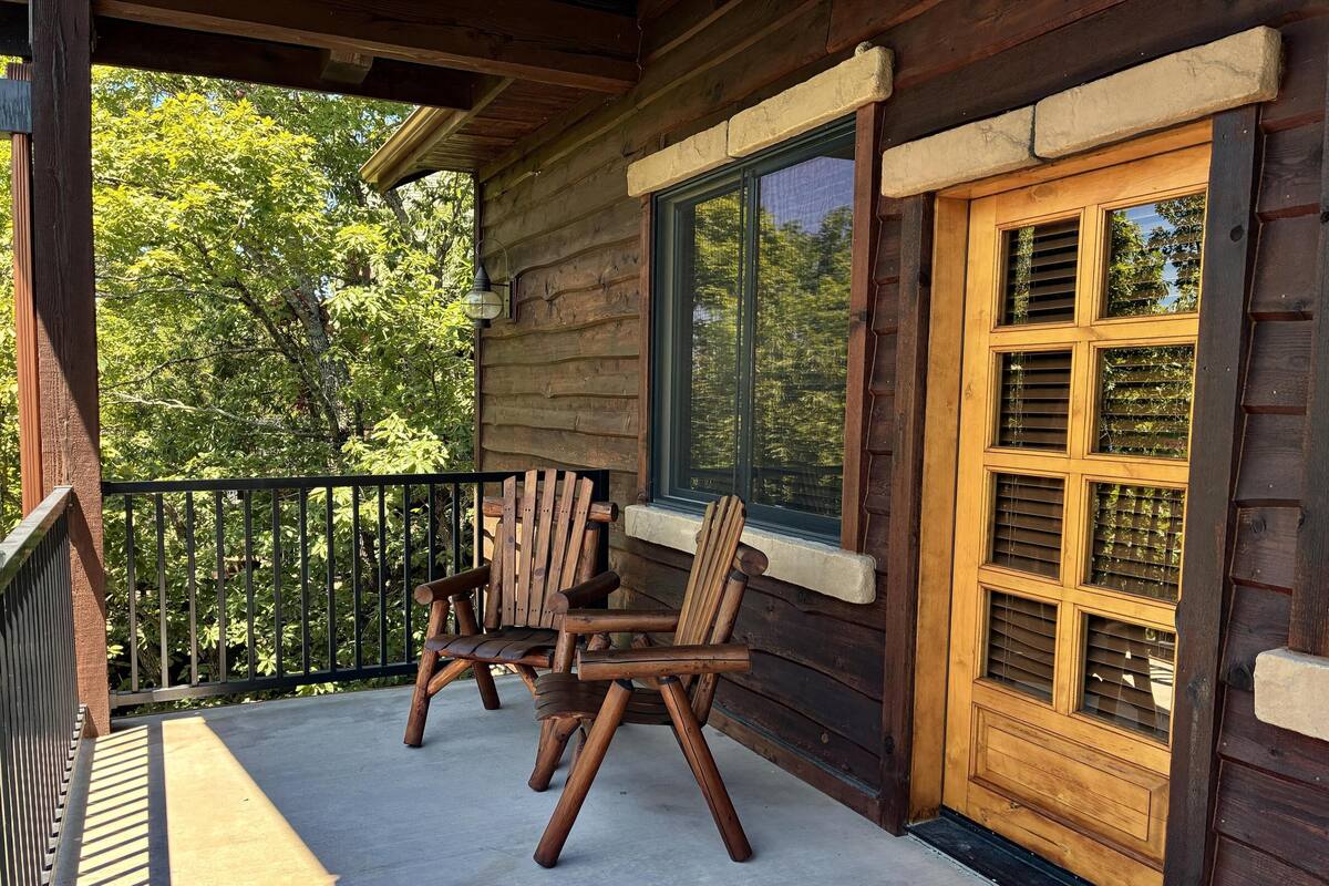 Una cabaña de madera con un porche, dos sillas de madera y una ventana con contraventanas.