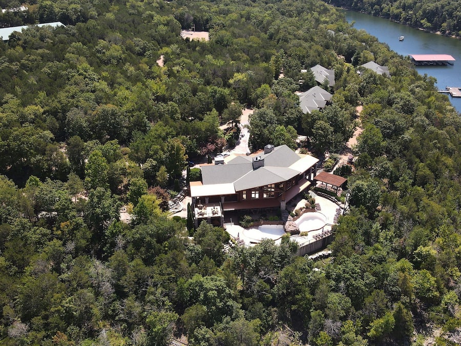 Una casa grande de un solo piso rodeada de un bosque frondoso, con un muelle que se adentra en un lago.