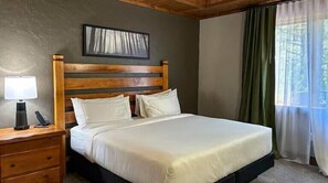 A bedroom with a wooden headboard, a bed with white bedding, a bedside table with a lamp, and a window with curtains. - Hilton Grand Vacations Club Stonewater Cove Shell Knob (Shell Knob)