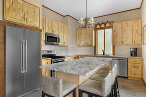 A kitchen with wooden cabinets, a stainless steel refrigerator, a microwave, a stove, a sink, and a marble countertop. - Hilton Grand Vacations Club Stonewater Cove Shell Knob (Shell Knob)