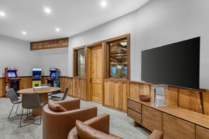 A room with a large flat-screen TV, wooden paneling, a table with chairs, and arcade games. - Hilton Grand Vacations Club Stonewater Cove Shell Knob (Shell Knob)