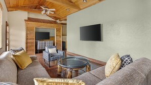 A spacious living area with a high wooden ceiling, a flat-screen TV mounted on the wall, and a comfortable seating arrangement including a sofa and a chair.