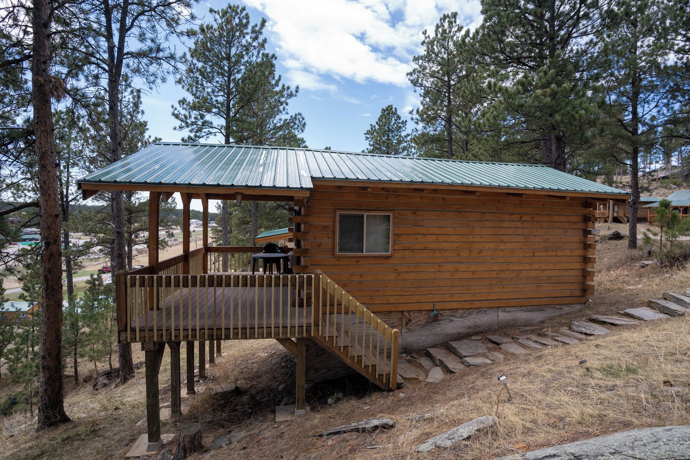 A wooden cabin with a metal roof, a deck, and a staircase leading to a window.