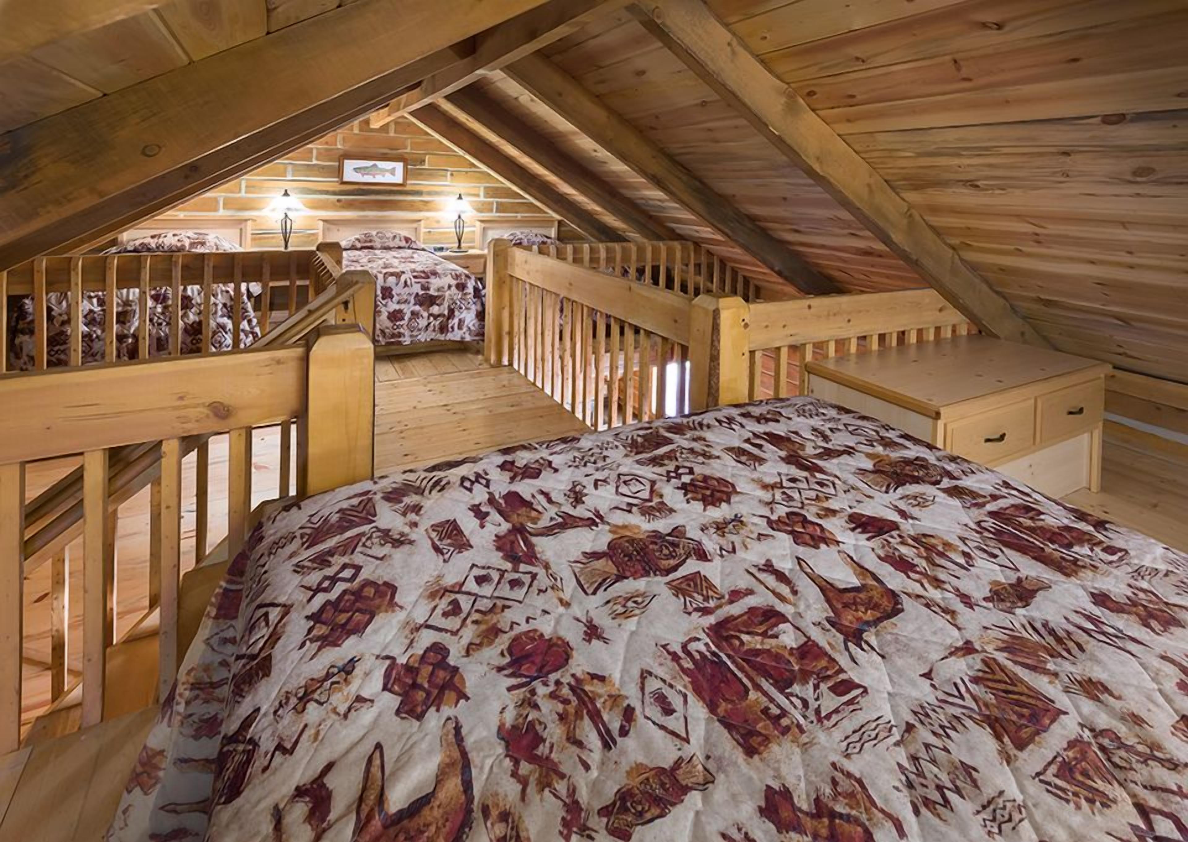 A wooden loft bedroom with a bed, a nightstand, and a dresser. There is a staircase leading to an upper level.